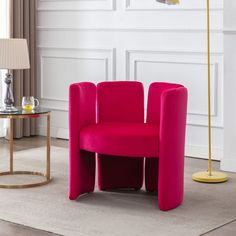 a pink chair sitting in front of a table with a lamp on top of it