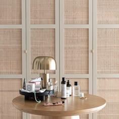 a wooden table topped with lots of bottles and makeup items next to a wall covered in bamboo panels