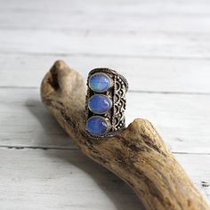 New Handcrafted Artisan Women's Chunky Blue Moonstone Ring Adjustable Front is approximately 1 5/8" H (from front top edge to front bottom edge) This hand-crafted ring is absolutely stunning. It is made of silver metal with three purplish blue oval stones set in silver casings with intricate hand worked raised metal lace detail. I believe the ring is made of sterling silver and I believe the stones are genuine moonstones, however I am not positive. It is heavy quality, and the workmanship is exquisite. The ring is roomy and fits a larger size finger. I believe it is approximate size 10 however the back can be adjusted to fit a larger finger. It's a gorgeous piece of artwork and is brand new without tags. The silver is tarnished, giving it a vintage antique patina. It could be cleaned, howe Bohemian Cabochon Moonstone Ring For Jewelry Making, Unique Blue Cabochon Moonstone Ring, Unique Blue Moonstone Cabochon Ring, Handmade Blue Bohemian Crystal Ring, Unique Blue Moonstone Jewelry, Bohemian Blue Moonstone Jewelry, Handmade Unique Blue Crystal Ring, Handmade Blue Crystal Ring With Unique Style, Artisan Blue Moonstone Jewelry