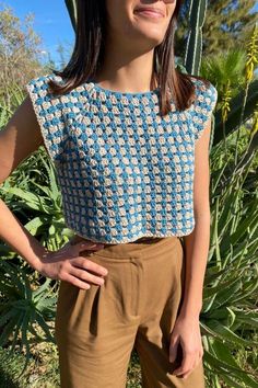 a woman standing in front of a cactus wearing a blue and white crochet top