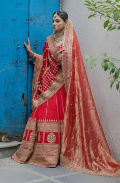 a woman in a red and gold lehenga standing by a blue wooden door