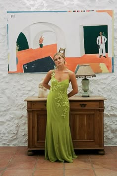 a woman in a green dress standing next to a painting