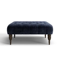 an upholstered foot stool with wooden legs and dark blue velvet finish, on a white background