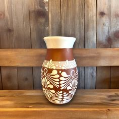 a brown and white vase sitting on top of a wooden bench