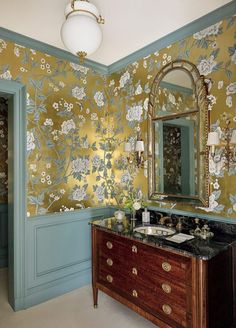 a bathroom with floral wallpaper and gold mirror above the vanity, along with an antique dresser