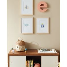 three framed pictures hang on the wall above a wooden table with books and toys in front of it