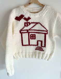 a white sweater with a red house on it