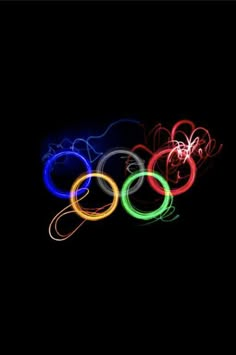 the olympic rings are lit up in the dark with colored light streaks on them, and there is no image here to provide a caption