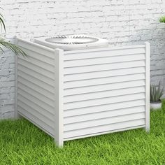 an air conditioner sitting in the grass next to a brick wall and potted plant