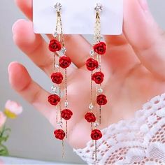 a pair of red roses dangling from long gold chain earrings with clear crystals on them