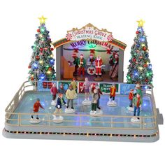 Plastic, animated figure for a Lemax display. Designed to look like an ice skating rink. There are a bunch of people skating around. There's a band on the stage in Christmas outfits and Santa hats. The sign on the stage reads Christmas Grove Skating Rink. Merry Christmas. There are two tall, decorated Christmas trees on either side of the stage. Skate Rink, Lemax Christmas Village, Lemax Village, Lemax Christmas, Stage Lights, Colonial Christmas, Village Display, Skating Rink, Holiday Village