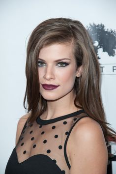 a woman with long brown hair wearing a black dress and purple lipstick on her lips