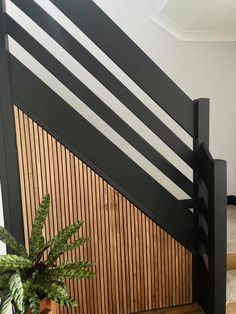 a plant in a pot sitting on the floor next to a stair case with black slats