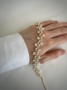 a woman's hand wearing a gold bracelet with pearls and flowers on it,