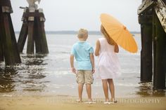 two children are standing on the beach with an umbrella over their heads and looking out at the water