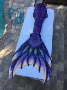 a purple and blue mermaid tail laying on top of a white mattress next to a swimming pool