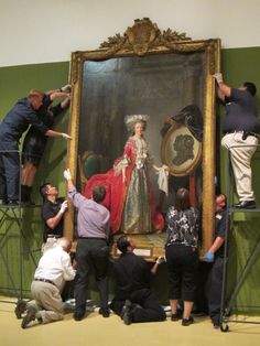 several people standing around a large painting in a room with other people working on it