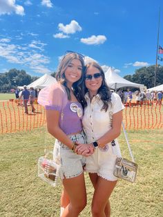 two young women standing next to each other in front of a tent at an outdoor event