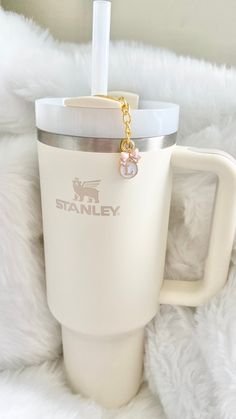 a white coffee cup with a gold chain on it sitting on top of a fluffy white blanket