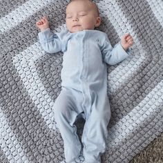 a baby laying on top of a blanket next to a gray and white afghan rug