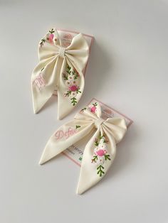 two white bows with pink flowers on them are sitting next to each other in front of a card