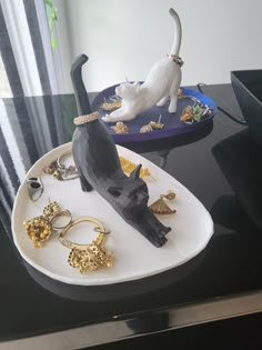 a cat figurine sitting on top of a white plate next to other jewelry