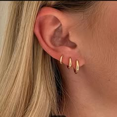 a woman wearing gold hoop earrings with two small curved posts on her ear, and the top half of her ear is shown