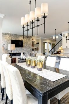 a dining room table with white chairs and lights hanging from the chandelier above it