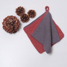 two knitted napkins next to pine cones on a white surface with red and gray accents