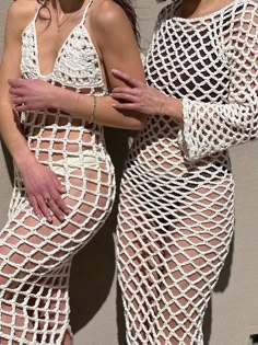 two women in white crochet swimsuits standing next to each other with their arms crossed