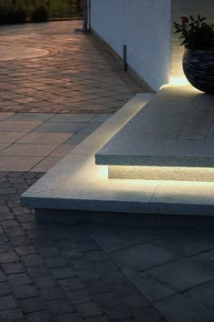 an illuminated planter sitting on the side of a building next to a brick walkway