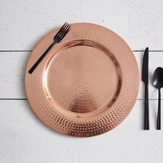 a copper plate with utensils and spoons next to it on a white wooden table