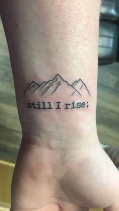 a small tattoo on the wrist that says still i rise with mountains in the background