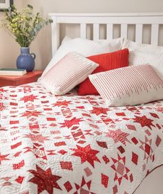 a bed with red and white pillows on top of it next to a vase filled with flowers