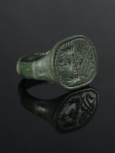 an ancient roman ring with leaves and flowers on the side, sitting on a black surface