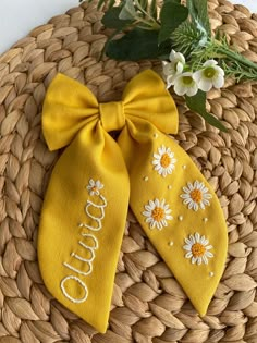 two yellow bow ties with daisies on them sitting on a woven basket next to flowers