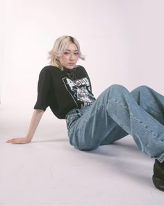 a woman sitting on the ground with her legs crossed and wearing black shoes, jeans and a t - shirt