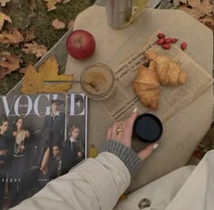 a person sitting on the ground next to an apple, croissant and magazine