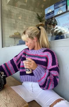 a woman sitting on a bench drinking from a cup in front of a store window