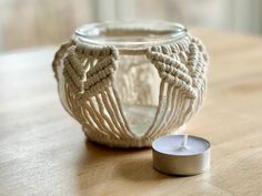 a white candle sitting on top of a wooden table next to a glass container with yarn wrapped around it