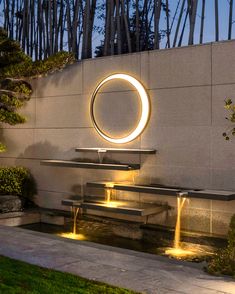 an outdoor fountain with lights in the shape of a circle next to a bench and table