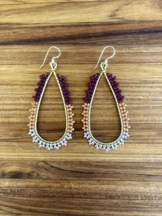 the beaded tear shaped earrings are made with gold and purple beads, on a wooden surface