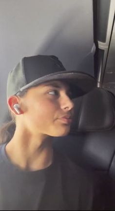 a woman wearing a baseball cap and ear buds sitting in the passenger seat of a car