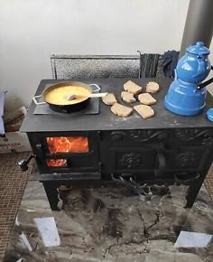 an old fashioned stove with food cooking on it and a blue kettle next to it