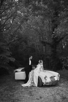 a bride and groom standing next to a convertible car in front of some trees at their wedding