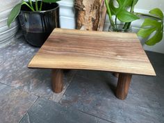 a small wooden table sitting on top of a stone floor next to potted plants