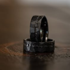 two wedding rings sitting on top of a wooden table next to each other with black diamond inlays