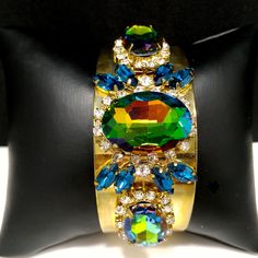 *Description: This is a gorgeous watermelon rhinestone crystal bracelet on a golden brass cuff which glitters and sparkles in the light. The vintage rhinestones are secured on a golden brass cuff and the reflective cuff adds additional sparkle to the bracelet. There is one large watermelon rhinestone in the center, surrounded by clear rhinestones and sapphire blue marquise cut rhinestones. On each side of the center stone are two more watermelon rhinestones, a little smaller in size, one on each Formal Earrings, Brass Cuff Bracelet, Vintage Christmas Gifts, Book Pieces, Brass Cuff, Blue Rhinestones, Crystal Bracelet, Sapphire Blue, Marquise Cut