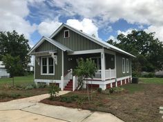 a small green house with white trim and red steps on the front porch is shown