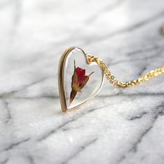 A single rose for the perfect gift for the unique gal in your life. A rose is encased in jewelry grade resin, within an antique bronze or gold plated heart bezel. The bezel is 1 1/2 inches in length and 1 1/4 inches in width- the matching chain is 24 inches. Chain is finished with a lobster clasp. Necklace will arrive attached to card shown in photos. Ready to be gifted! This necklace is custom made. Just like nature, no two will be exactly alike! Let me assure you, though, that we replicate eac Rose-colored Heart-shaped Jewelry For Gifts, Rose Heart-shaped Jewelry Gift, Rose Heart-shaped Jewelry For Gift, Heart-shaped Rose Colored Jewelry For Gift, Heart-shaped Rose Jewelry For Gift, Rose Heart-shaped Necklace For Gift, Rose Jewelry For Valentine's Day, Valentine's Day Gift Jewelry With Rose Design, Rose Design Rose Gold Jewelry For Anniversary